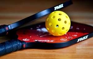 yellow pickleball ball between 2 red paddles