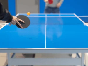 person hitting table tennis ball, blue table