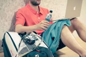 man sitting with backpack and squash equipment
